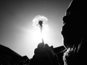 Low angle view of girl blowing dandelion against sky