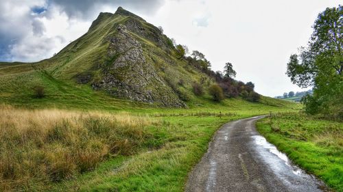 Road amidst grassy field against sky