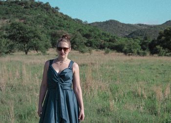 Portrait of young woman standing on grassy field against mountains