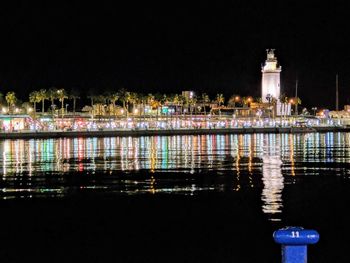 Illuminated buildings by lake against clear sky at night