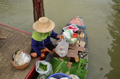 High angle view of vendor arranging objects in boat for floating market