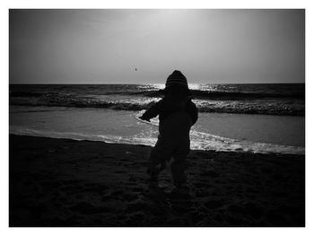 Rear view of silhouette boy standing on beach against clear sky