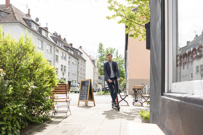 Businessman using e-scooter on pavement in the city