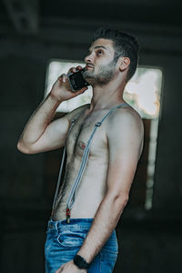 Midsection of shirtless young man holding camera