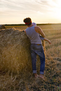 Father and son in t-shirts standing next to a haystack on a sloping field during sunset