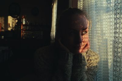 Young woman looking away while standing by window at home