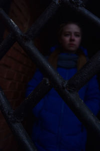 Low angle view of boy looking through metal fence