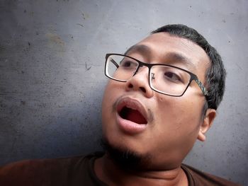 Close-up portrait of man wearing eyeglasses against wall