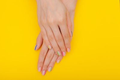 Close-up of woman with colorful fingernails on yellow background