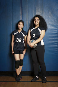 Portrait of girls standing against blue wall at volleyball court