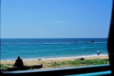 People sitting on beach against clear blue sky