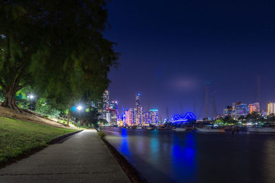 Illuminated buildings by river against sky in city at night