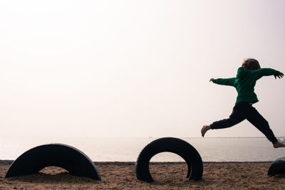 Boy playing on tire at beach against clear sky