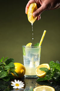 Hand squeezing lemon in lemonade on dark background. vertical format.