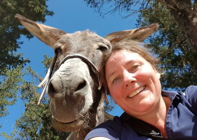 Low angle view portrait of smiling woman taking selfie with donkey