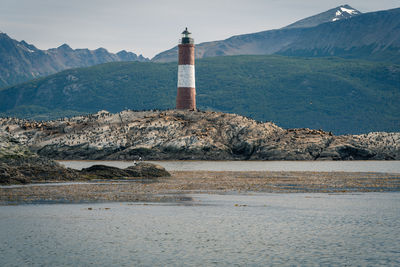 Lighthouse by sea against mountain and sky