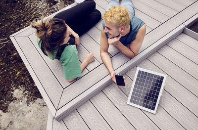 Young couple lying on patio charging mobile phone through solar energy