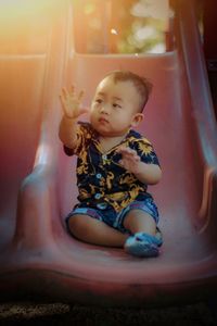 Cute baby boy sitting on slide in playground