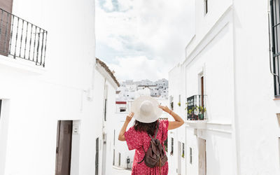 Back view of unrecognizable female tourist with raised arms on narrow street between old houses in greece