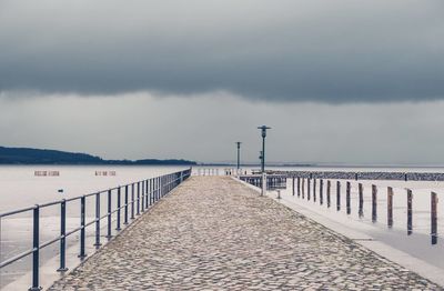 Empty pathway amidst lake against sky