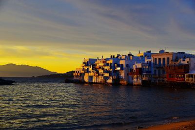 Buildings by sea against sky during sunset