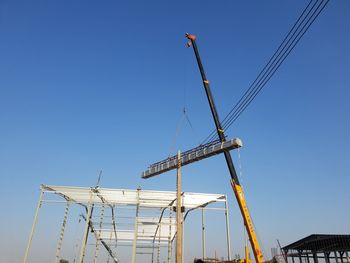 Low angle view of cranes against clear blue sky
