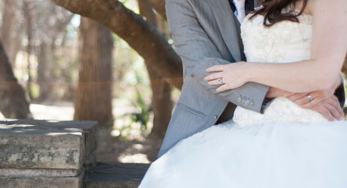 Midsection of bride and groom embracing by retaining wall at park