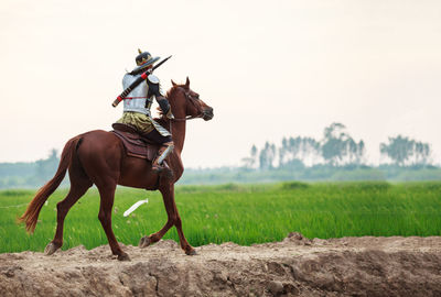 Horse riding motorcycle on field against sky