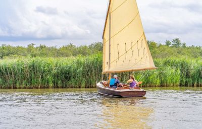 People sitting on sailboat by lake against sky