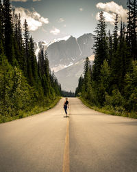 Rear view of woman skateboarding on road against mountain