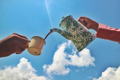 Low angle view of hand holding umbrella against sky