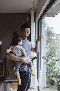 Father pointing out of window while carrying male toddler at home