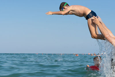 Boy jumping in sea against clear sky