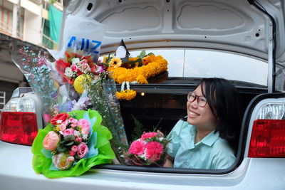 Happy young woman with bouquets sitting in car trunk