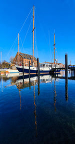 Sailboats moored at harbor against clear blue sky