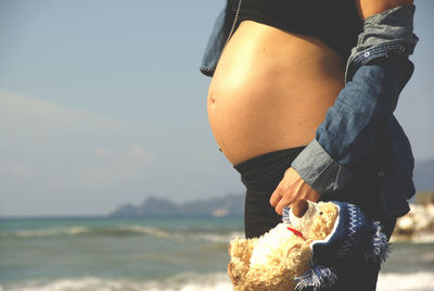 Midsection of pregnant woman holding stuffed toy at beach