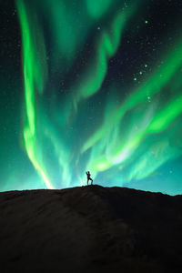 Low angle view of people standing on landscape against sky at night