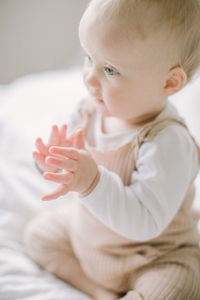 Baby girl clapping hands on bed in soft light