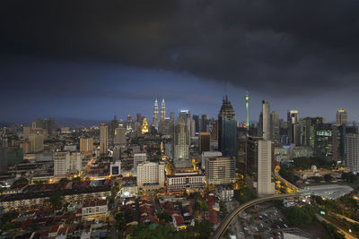 Distant view of petronas tower against cloudy sky in city at dusk