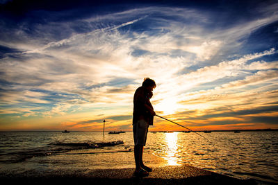 Silhouette person standing on beach against sky during sunset