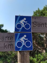 Close-up of road sign on wooden post against clear blue sky