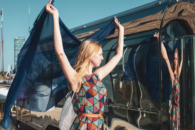 Woman holding blue scarf standing against bus