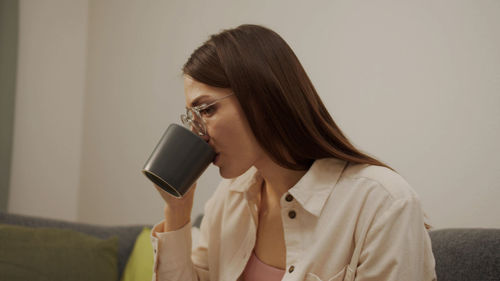 Portrait of young woman drinking coffee cup against wall