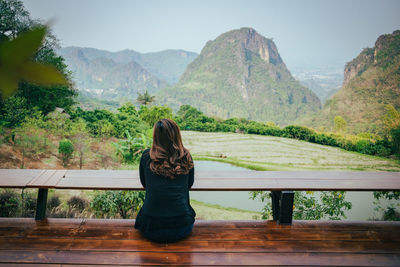 Rear view of woman sitting on mountain against sky