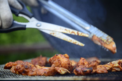 Close-up of hand holding scissors over roasted food on barbecue grill