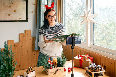 Female florist blogger making winter ikebana with pine branches, candle and christmas decorations