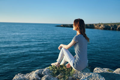 Woman sitting on rock looking at sea against sky