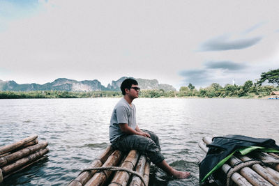 Man sitting on wooden raft over lake against sky