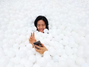 Happy woman amidst white balls using phone in pool