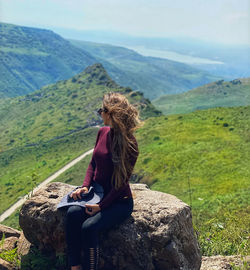 Man sitting on rock looking at mountains against sky